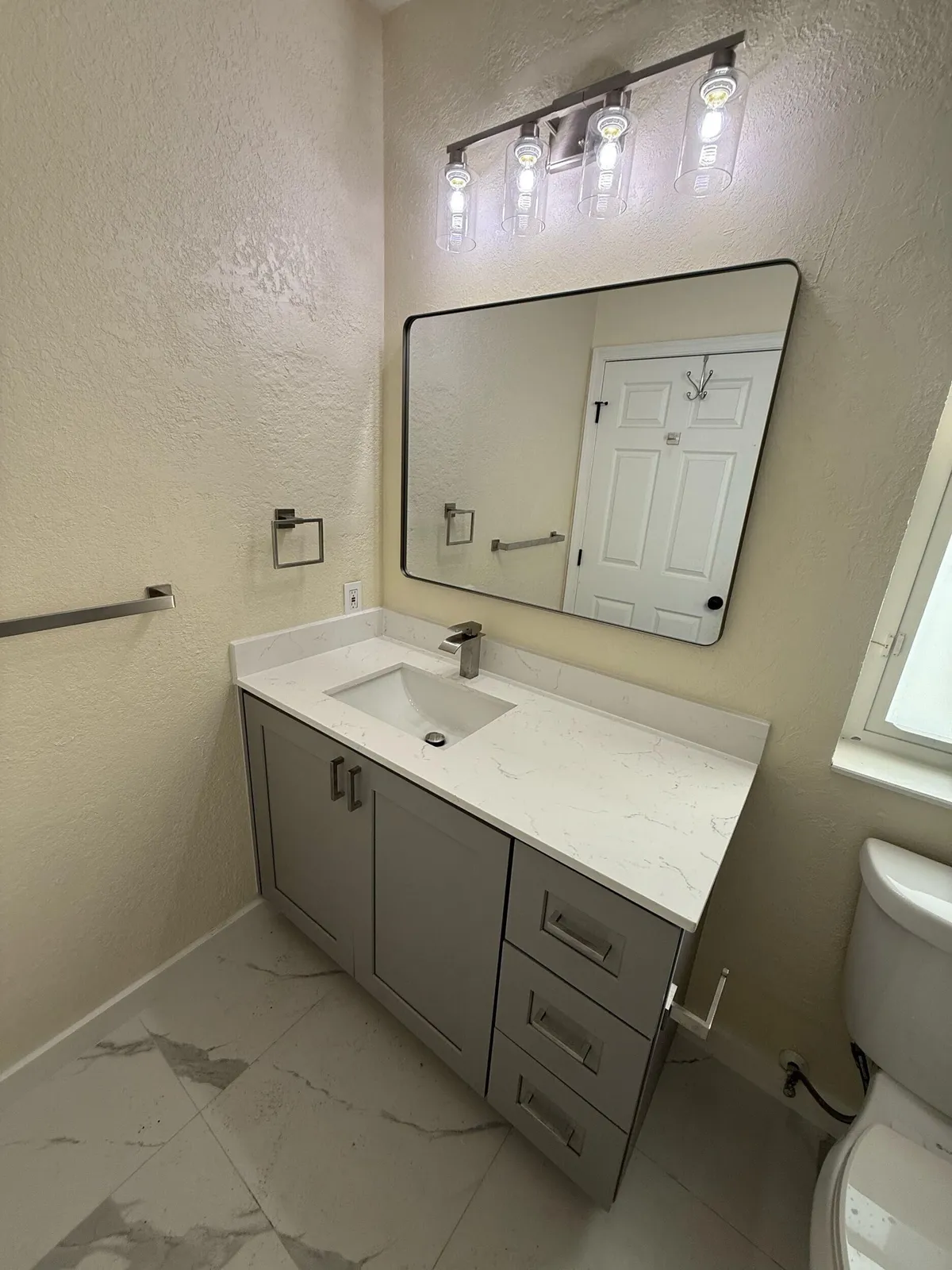 Finished bathroom remodel with a new vanity, mirror and marble-look tile, by MGS